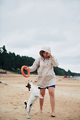 Image showing Young woman in jacket playing with dog on beach