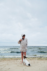 Image showing Woman in jacket looking at dog near sea