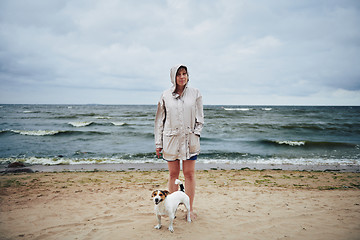 Image showing Woman in jacket looking at dog near sea