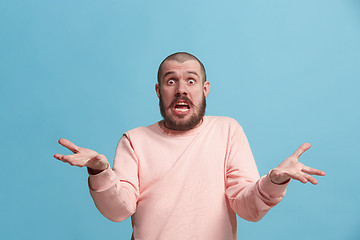 Image showing Beautiful male half-length portrait isolated on blue studio backgroud. The young emotional surprised man