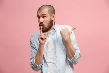 Image showing The young man whispering a secret behind her hand over pink background