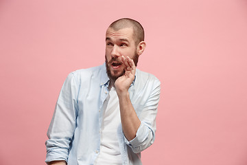 Image showing The young man whispering a secret behind her hand over pink background