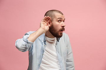 Image showing The young man whispering a secret behind her hand over pink background