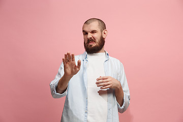 Image showing Young man with disgusted expression repulsing something, isolated on the pink