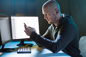 Image showing hacker with smartphone and computers in dark room