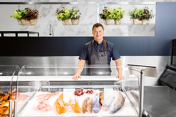 Image showing male seller with seafood at fish shop fridge