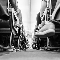 Image showing Low agle view of passenegers commercial airplane aisle with passenegers sitting on their seats while flying. Black and white photo.