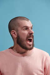 Image showing The young emotional angry man screaming on blue studio background