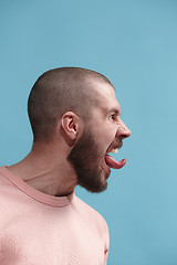 Image showing The young emotional angry man screaming on blue studio background