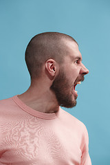 Image showing The young emotional angry man screaming on blue studio background