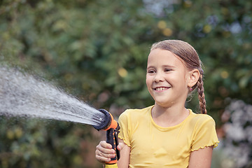 Image showing Happy little girl pouring water from a hose.