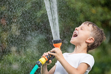 Image showing Happy little boy pouring water from a hose.