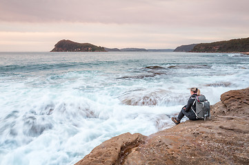 Image showing Woman sitting by the ocean letting waves lap at her feet