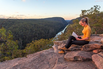 Image showing A woman sitting on a rock reading in nature