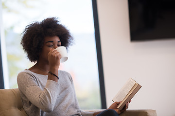 Image showing black woman reading book  in front of fireplace