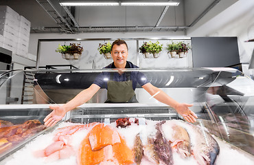 Image showing male seller showing seafood at fish shop fridge