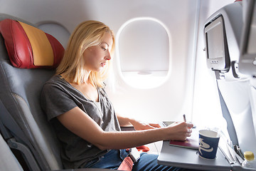 Image showing Casual woman flying on commercial passengers airplane, filling in immigration form.