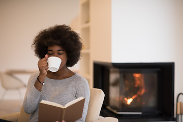 Image showing black woman reading book  in front of fireplace