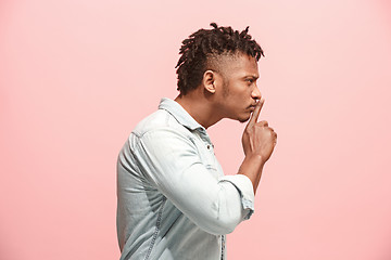 Image showing The young man whispering a secret behind her hand over pink background