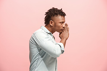 Image showing The young man whispering a secret behind her hand over pink background