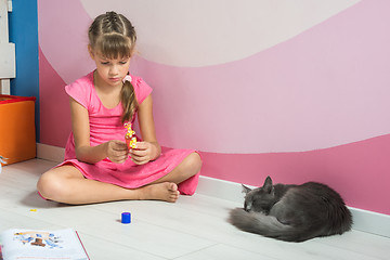 Image showing A girl is making figures out of colored paper, a domestic cat is sleeping nearby