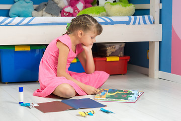 Image showing A girl chooses a hand-made article in her book to make it from a colored paper