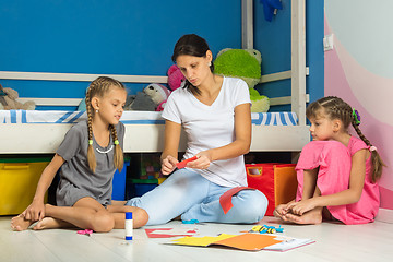 Image showing Mom explains to daughters how correctly to cut out figures from colored paper