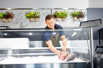 Image showing male seller putting trout to fridge at fish shop