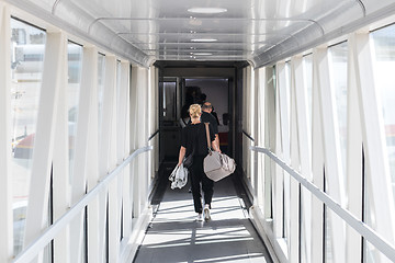 Image showing Female passenger carrying the hand luggage bag, walking the airplane boarding corridor.