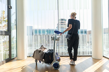 Image showing Casual woman on airport terminal talking on the cell phone, waiting for flight departure with luggage on trolley cart.