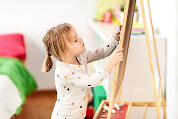 Image showing happy little girl drawing on chalk board at home