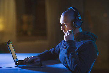 Image showing hacker in headset typing on laptop in dark room