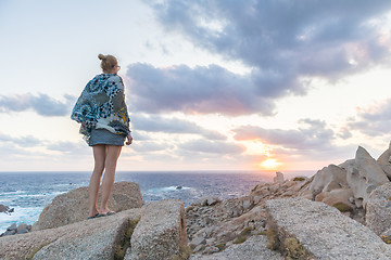 Image showing Solo young female traveler watches a beautiful sunset on spectacular rocks of Capo Testa, Sardinia, Italy, a popular summer traveling destination in Europe.