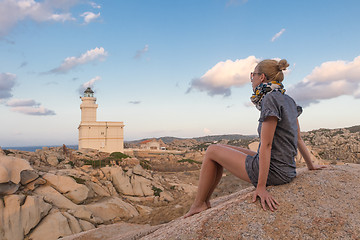 Image showing Solitary young female traveler watches a beautiful sunset over lighthouse and spectacular rock formations of Capo Testa, Sardinia, Italy.