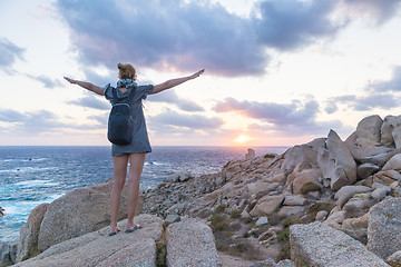 Image showing Female traveler, arms rised to the sky, watches a beautiful sunset on spectacular rocks of Capo Testa, Sardinia, Italy.