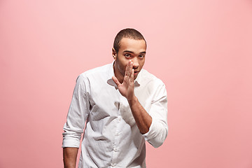 Image showing The young man whispering a secret behind her hand over pink background