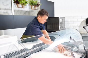 Image showing male seller putting trout to fridge at fish shop