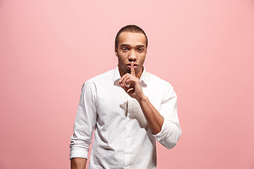 Image showing The young man whispering a secret behind her hand over pink background