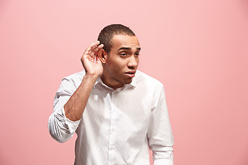 Image showing The young man whispering a secret behind her hand over pink background