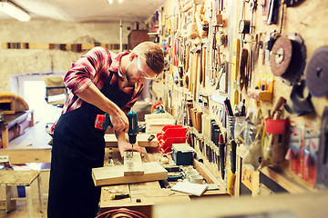 Image showing carpenter with drill drilling plank at workshop