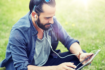 Image showing man with earphones and tablet pc sitting on grass