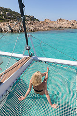 Image showing Woman relaxing on a summer sailing cruise,lying in hammock of luxury catamaran near picture perfect white sandy beach on Spargi island in Maddalena Archipelago, Sardinia, Italy.