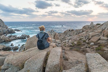 Image showing Solo young female traveler watches a beautiful sunset on spectacular rocks of Capo Testa, Sardinia, Italy.