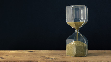 Image showing a hourglass on a wooden underground with black background