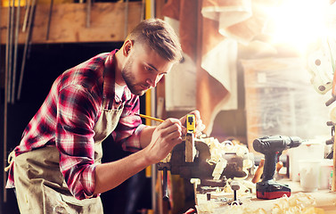 Image showing carpenter with ruler measuring plank at workshop