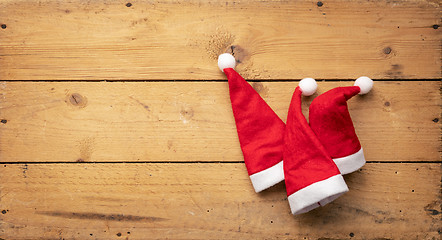 Image showing three red Santa Claus hats with wooden background