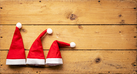 Image showing three red Santa Claus hats with wooden background