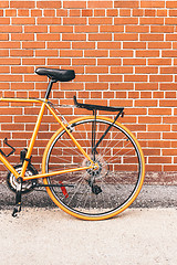 Image showing Stylish orange bicycle near red brick wall