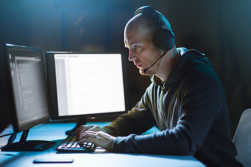 Image showing hacker with computer and headset in dark room