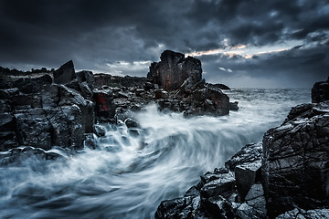 Image showing Moody dramatic skies and large waves crash onto coastal rocks